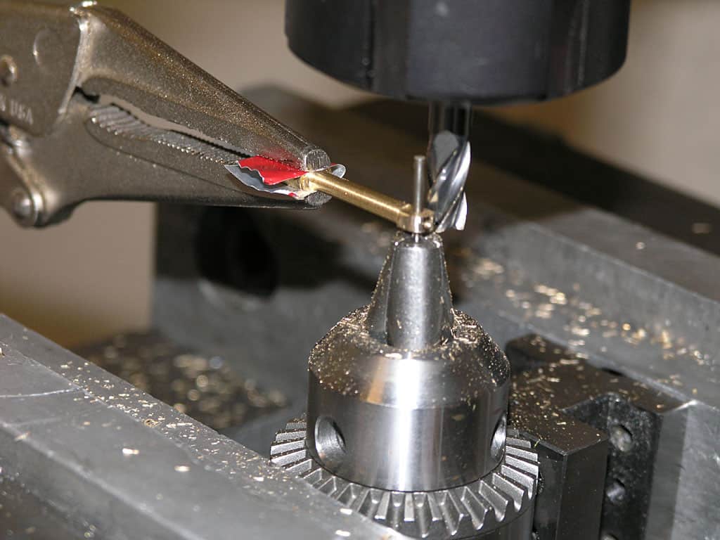 A silver drill bit with red and white label being inserted into a chuck with metallic teeth.