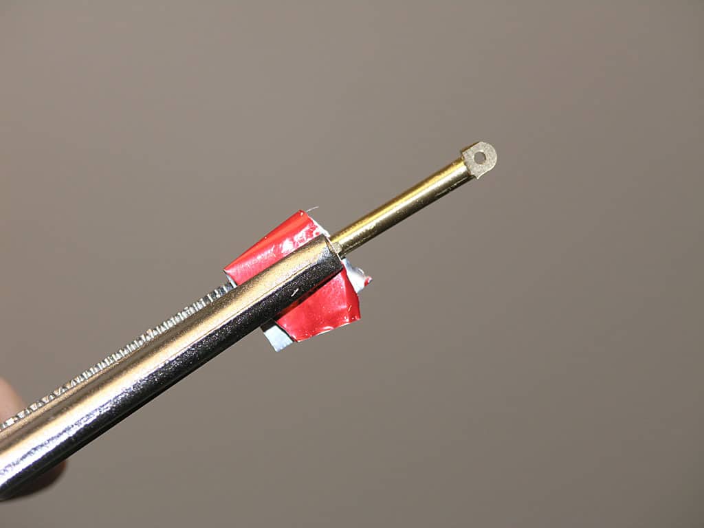 Antique brass rod with red tape wrapped around it, featuring a hole at one end.