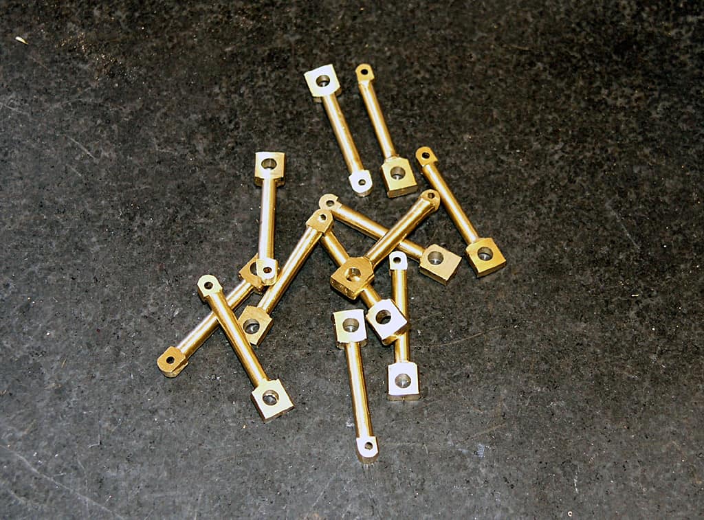 Small gold-colored metal rods with circular holes and square bases, arranged on a dark gray surface.