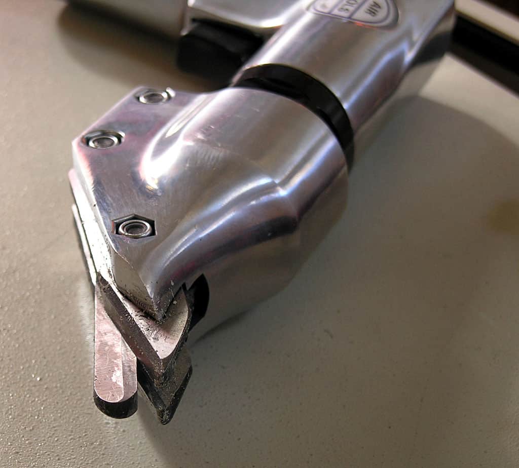 A silver metal tool with a flat top and curved bottom, featuring sharp edges and a pointed tip.