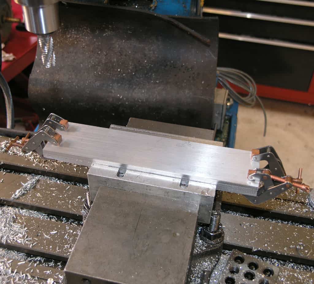 Large metal piece on machining machine table with tools and equipment.