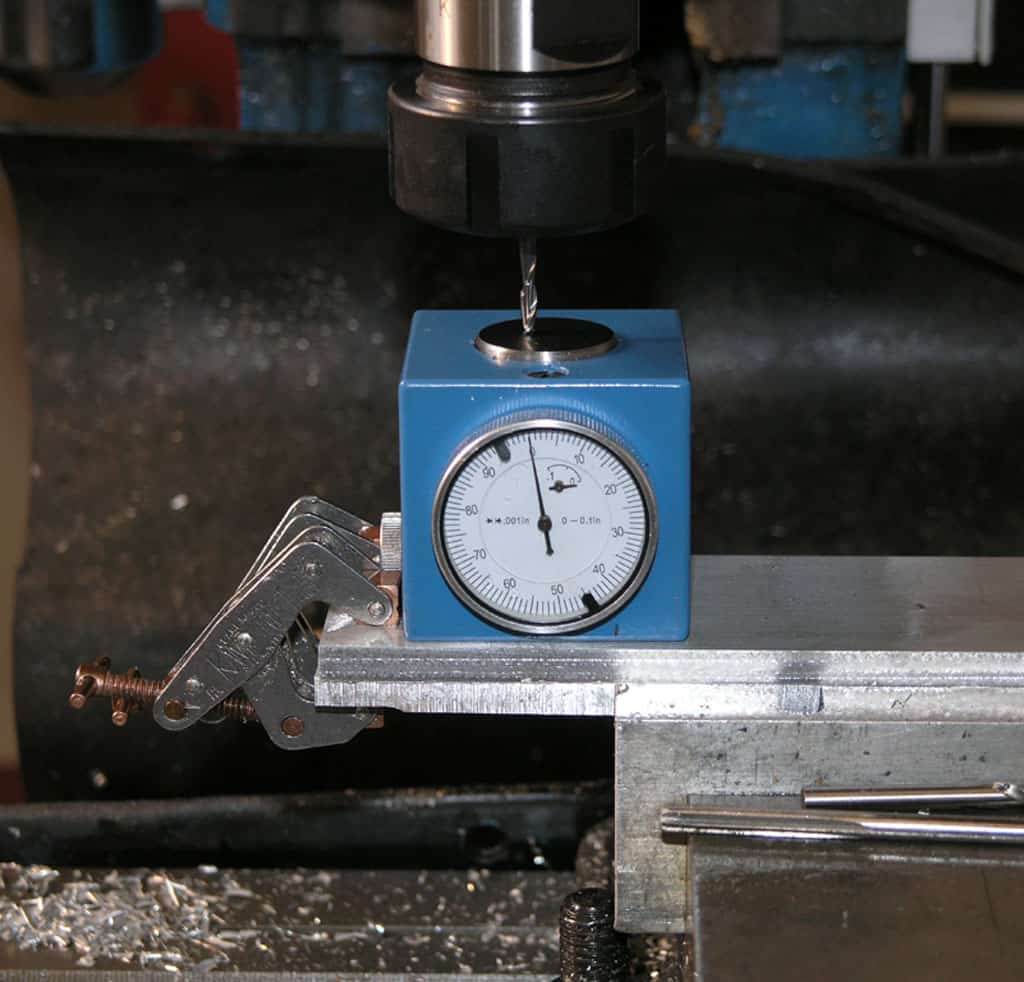 A blue dial gauge attached to an aluminum vise in a machine shop.