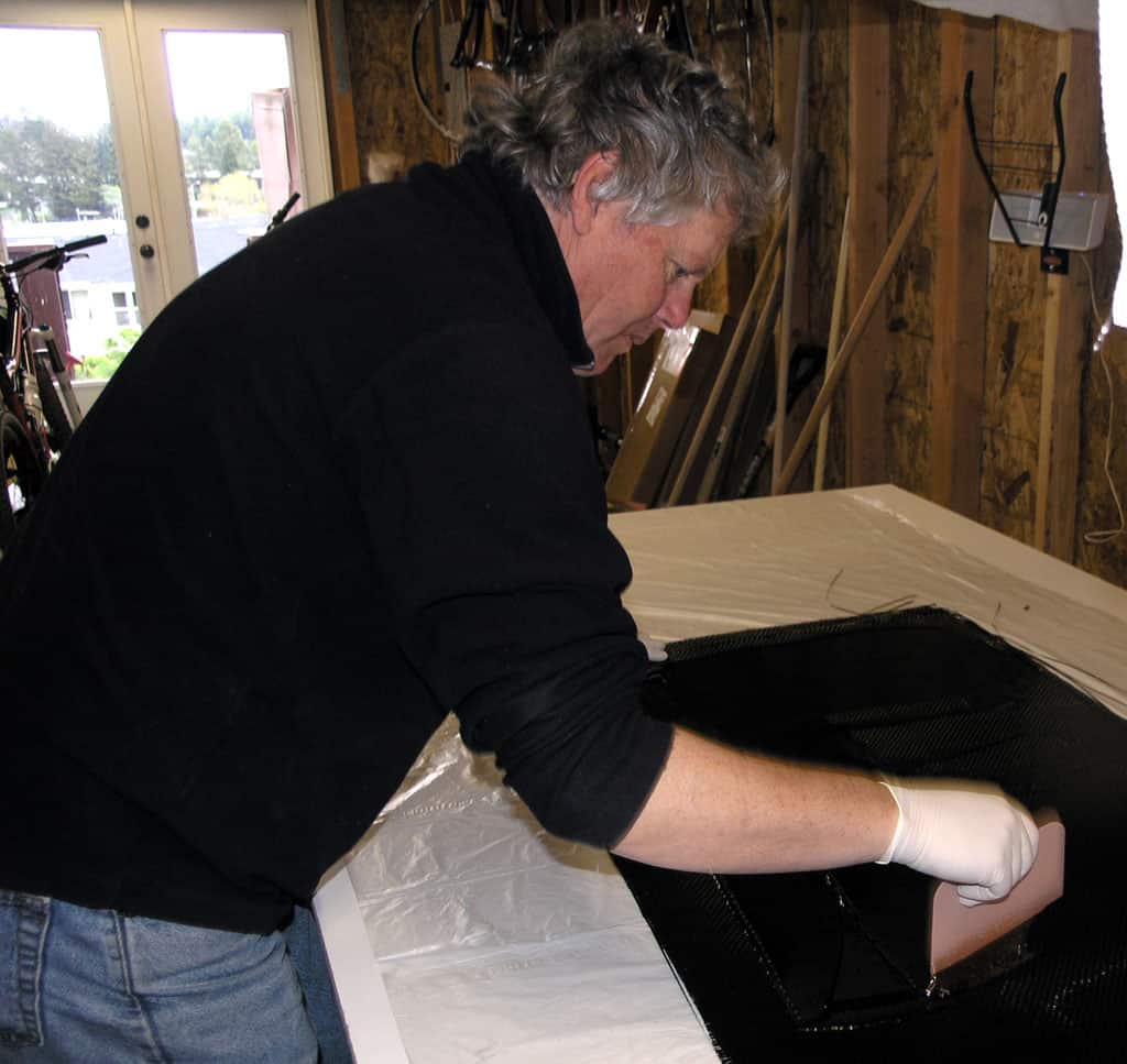 Man working with carbon fiber material in workshop setting.