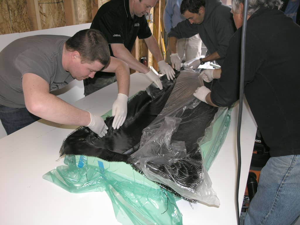 Men working together in a workshop, laying down a large piece of black material on a white surface.