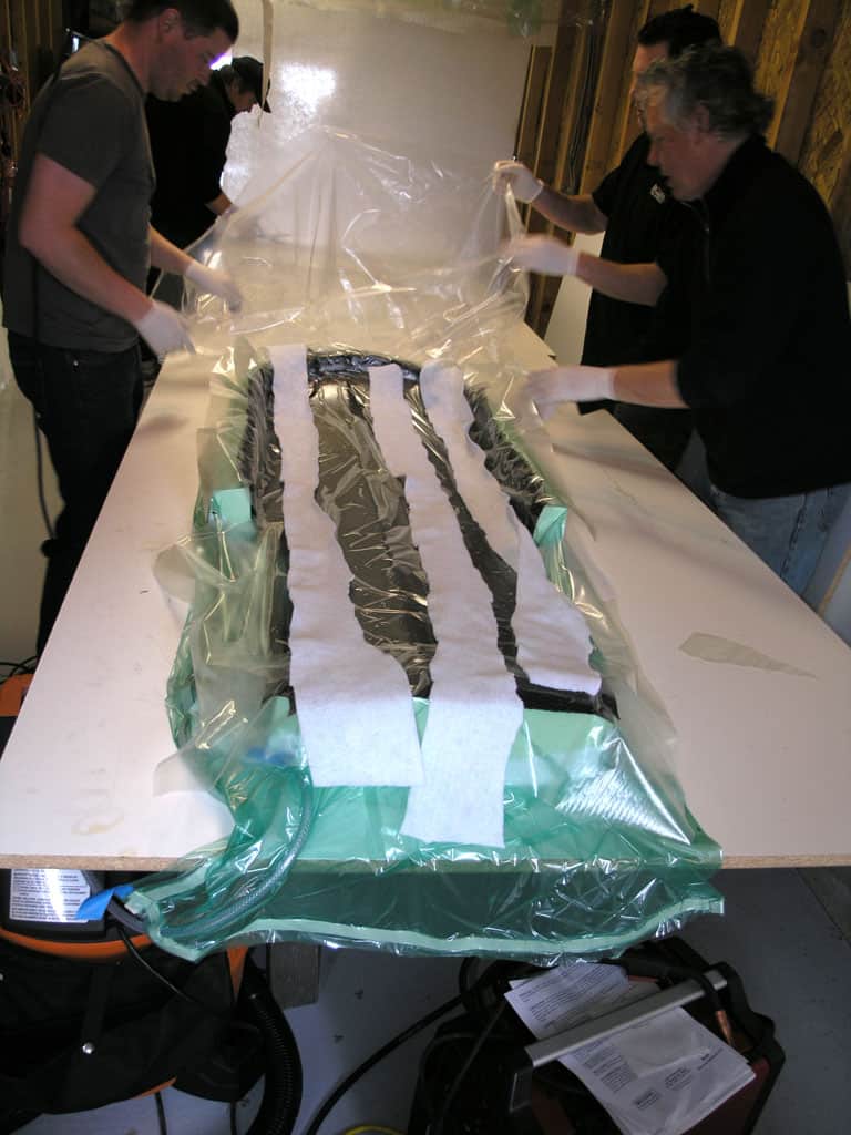 Individuals preparing an object for vacuum bagging process with plastic sheeting and vacuum hose.