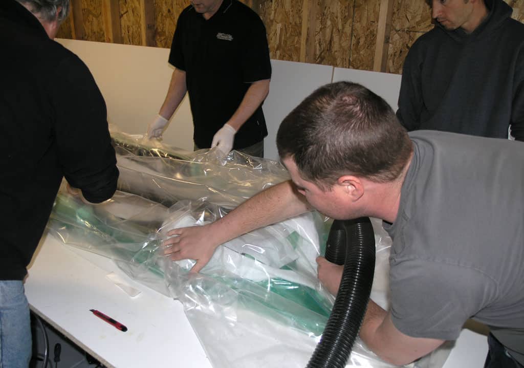 Men gathered around a white table, intently focused on an object wrapped in plastic wrap.
