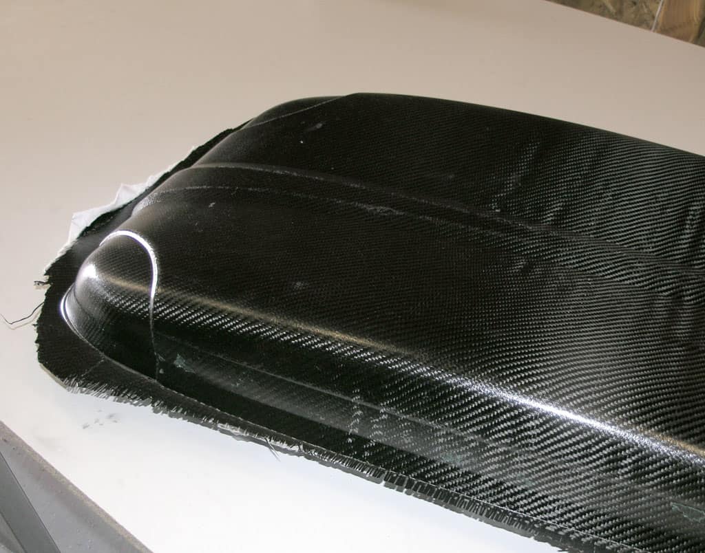 Carbon fiber part with glossy finish and rough edges on a workshop background