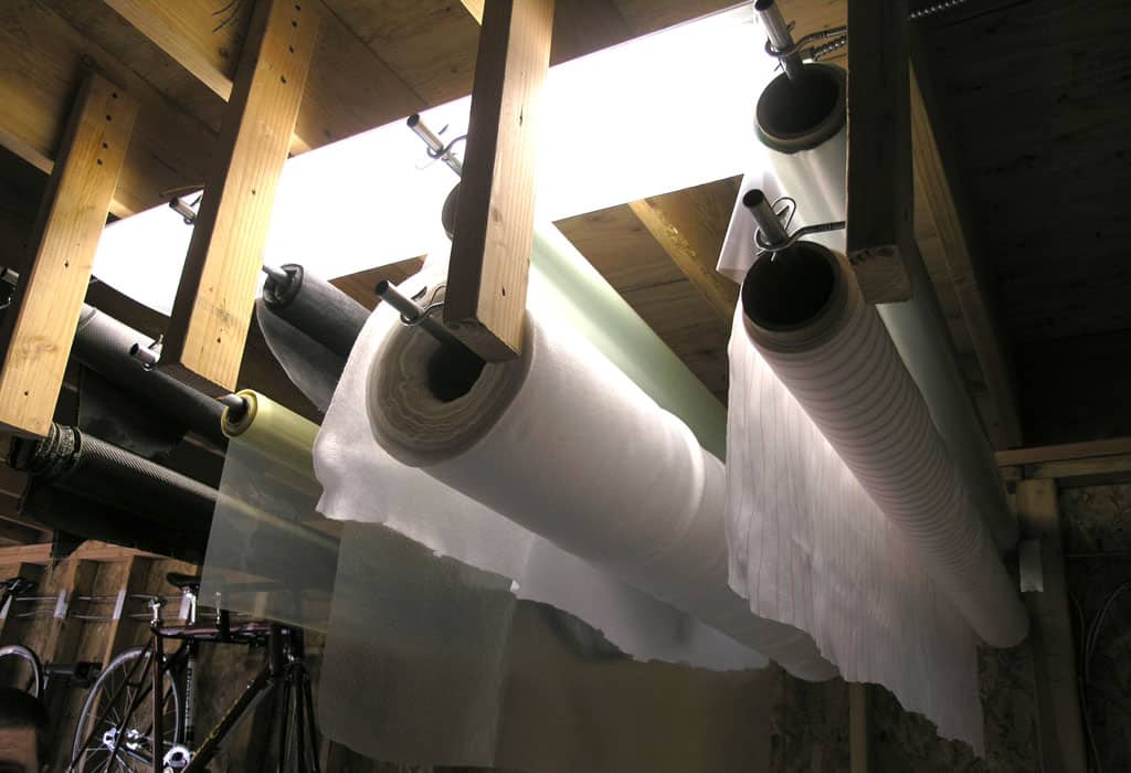 Wooden ceiling with exposed beams supporting rolls of transparent plastic sheeting on metal brackets.
