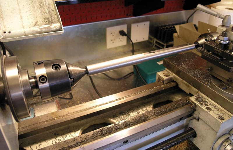 Lathe work area cluttered with metal shavings, featuring a metal shaft and cone-shaped object.