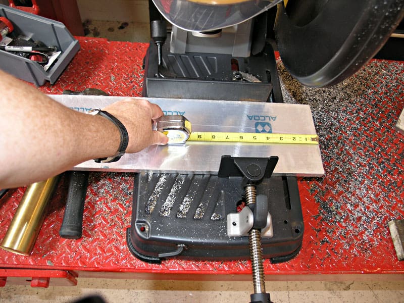 Hand holding a silver object on a metal plate with blue markings, over a red workbench with tools.