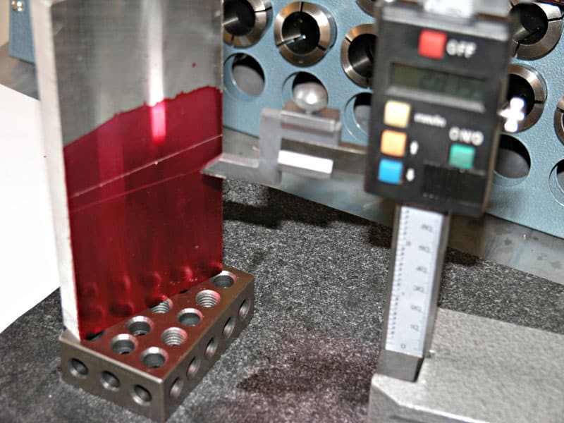 A digital caliper on a gray surface surrounded by various metal parts and objects.