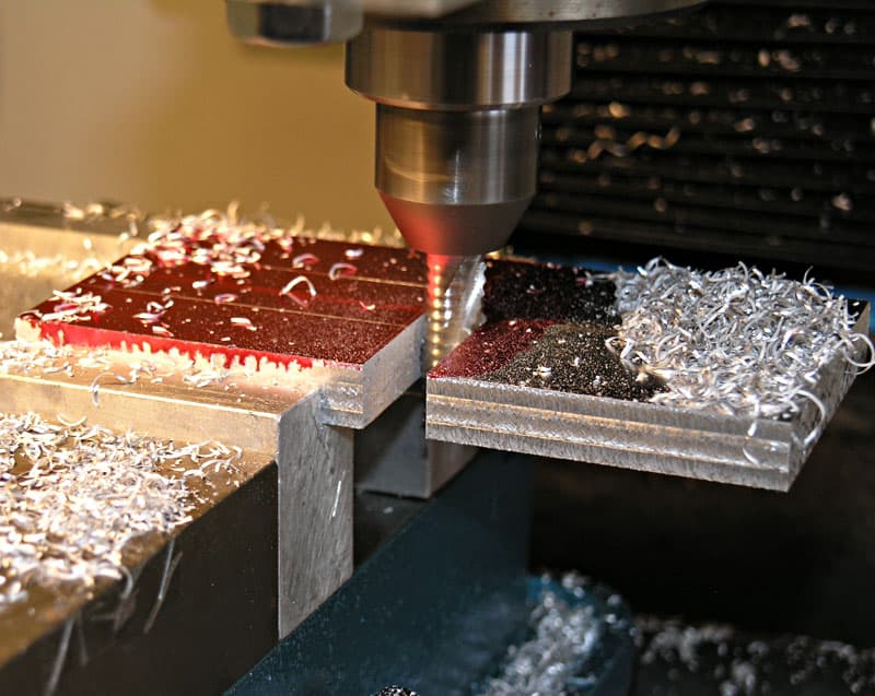 Metal cutting tool positioned above two pieces of metal with red and black surfaces, tip poised for cutting.