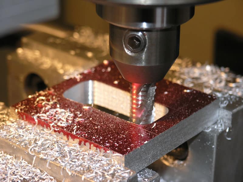 Metal cutting tool in action, surrounded by shavings and debris on a red square metal object.