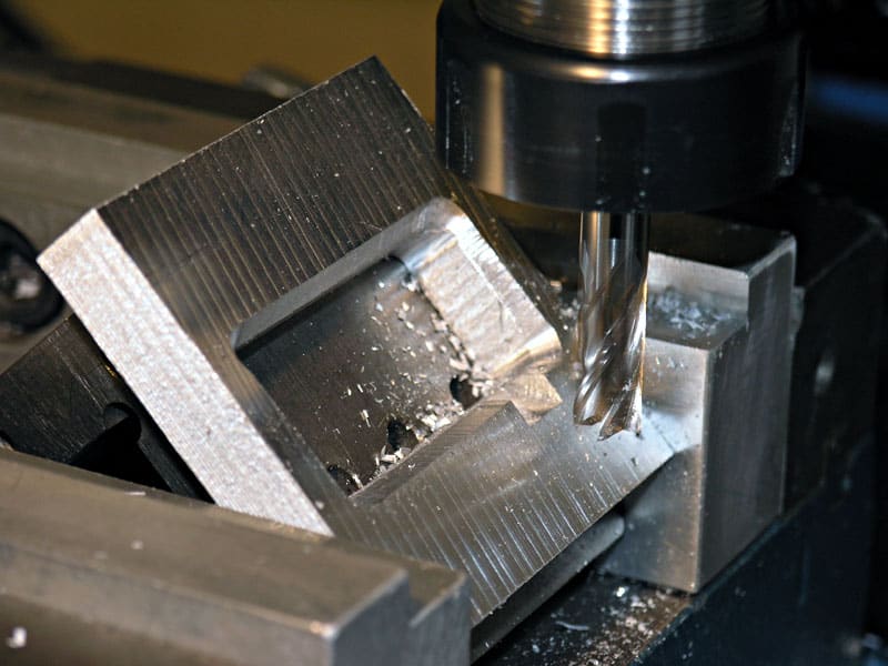 A milling machine in an industrial environment with a black cylindrical component on its surface featuring grooves.