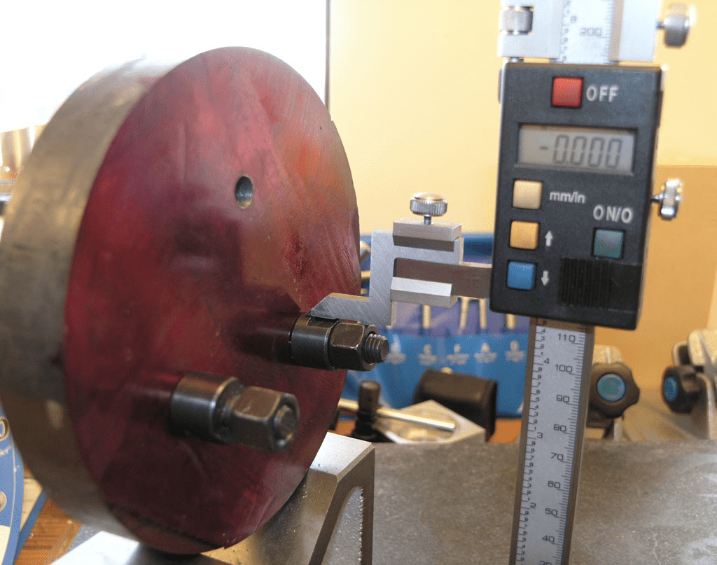 Digital caliper on workbench measuring metal object diameter.
