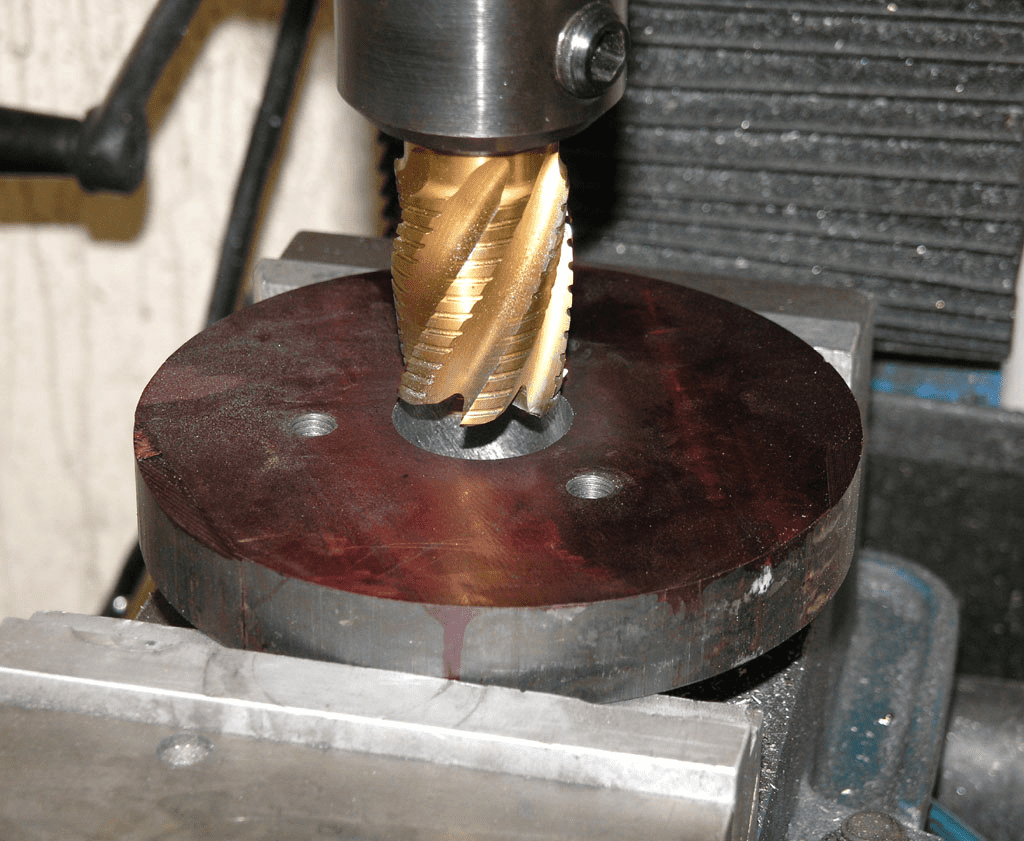 Metalworking tool on dark red circular base with gray metal frame against white wall.