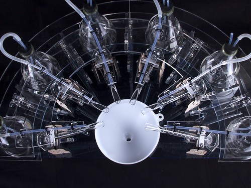 Clear plastic or glass object with multiple holes and tubes, featuring white circular components and blue tubing.