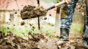 A person outdoors using a shovel in the ground amidst dirt and debris.