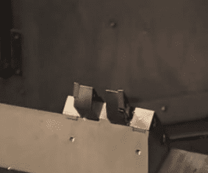 Metal object with two rectangular cutouts on top surface against a dark background.