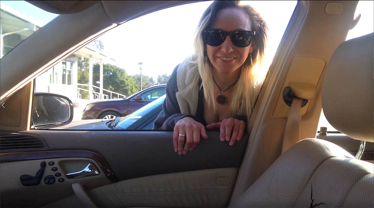 Woman leaning out of a passenger window, smiling and wearing sunglasses.