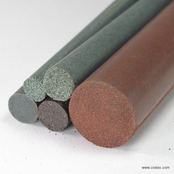Three cylindrical abrasive rods with rough surfaces and different colors and textures, arranged diagonally on a white background.