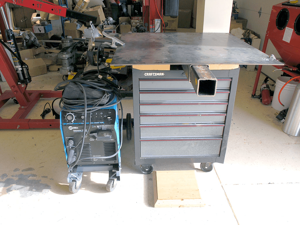 A cluttered workshop with a welding machine, metal cutting saws, and a CNC milling machine.