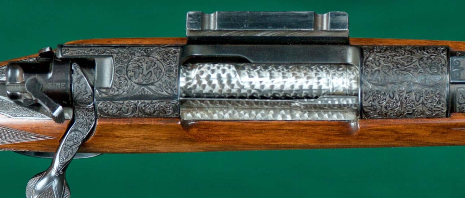Detailed image of a rifle's bolt action with intricate metal engravings and floral-patterned bolt handle.