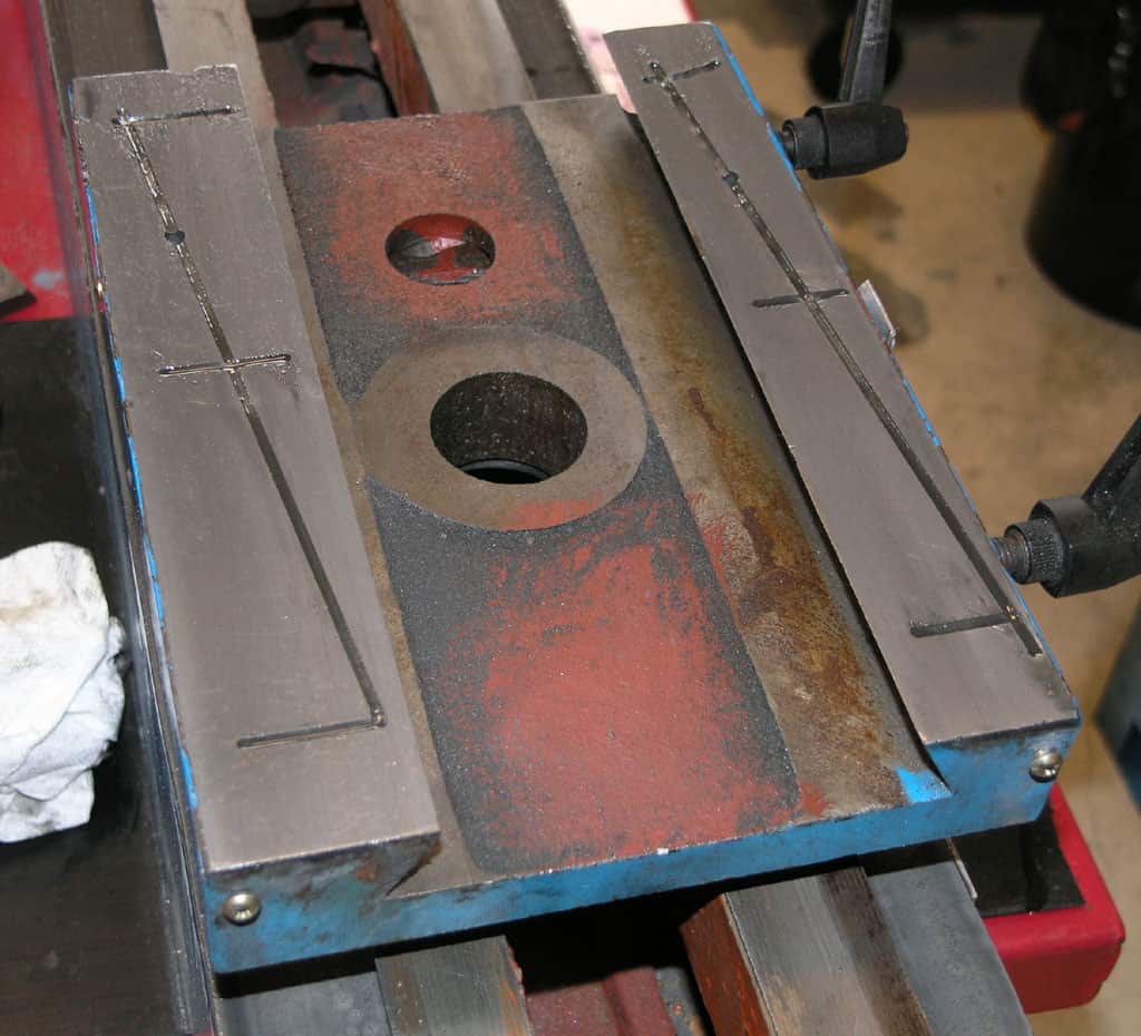 Large metal object with 2 circular holes, blue base, and red surface on a workbench.