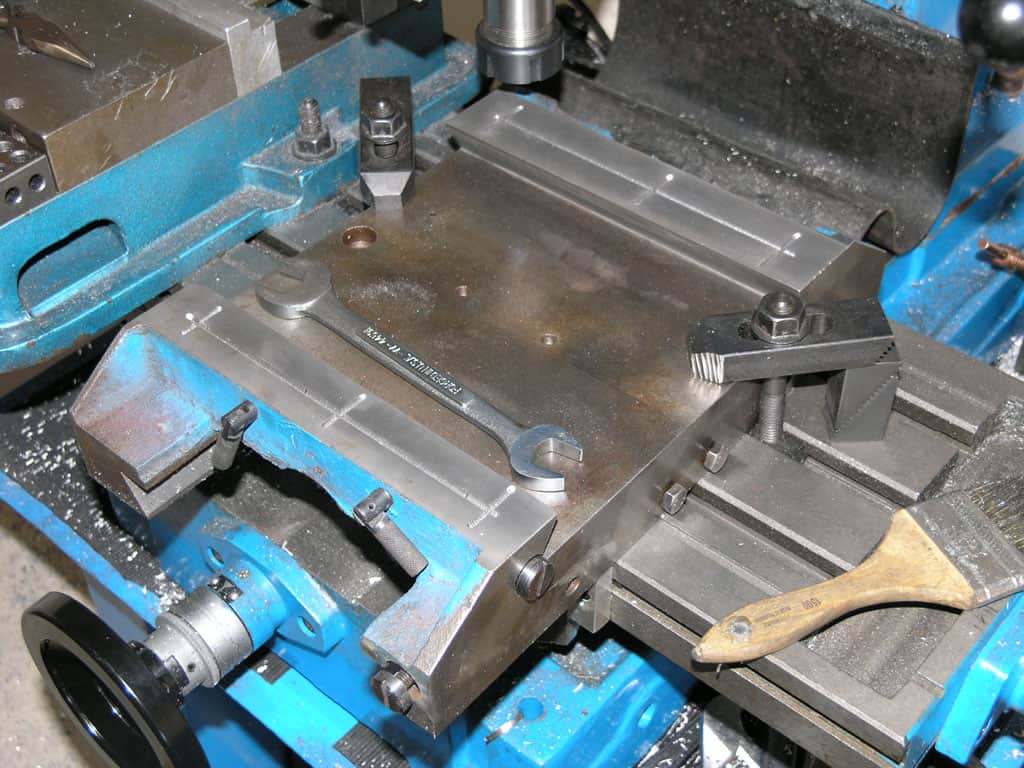 Blue and black metalworking vise with wooden handle in a workshop or factory setting.