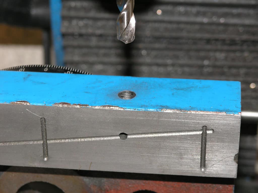 Metal workpiece on a drill press in a workshop setting.