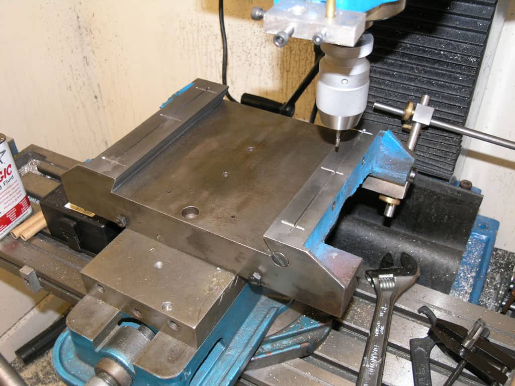 Metalworking machine shop workspace with well-organized clutter of machinery and tools surrounding large metal plate.