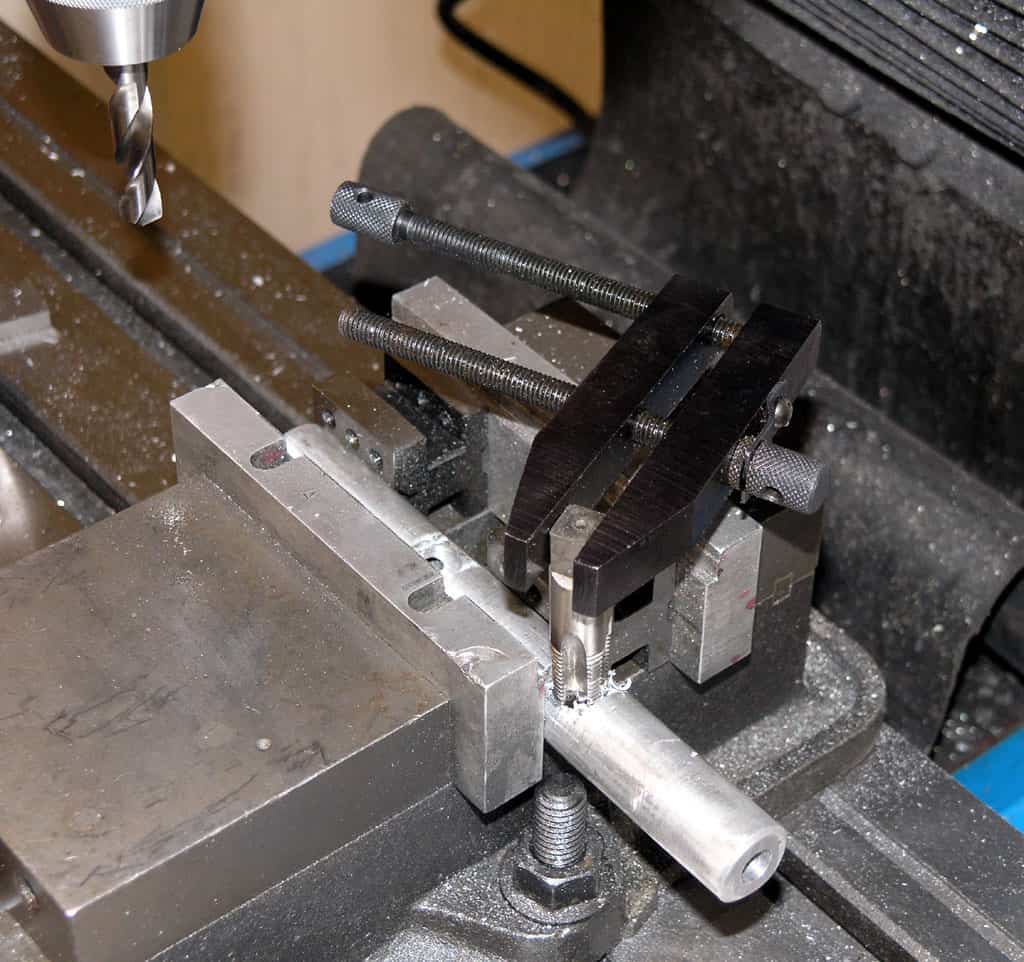 Metalworking setup with drill bit and tools on a drill press or milling machine, surrounded by metal shavings and dust.