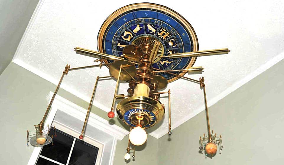 Astronomical clock with blue circular dial and gold accents displaying months and zodiac signs, with pendulums and planet globes.