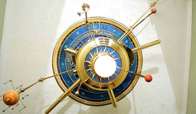 Ornate blue and gold astronomical clock with sun at center, featuring concentric rings with Roman numerals.