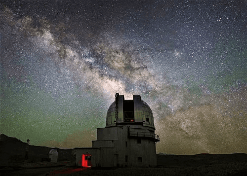 Milky Way galaxy set against a starry night sky with a distant building in the foreground.