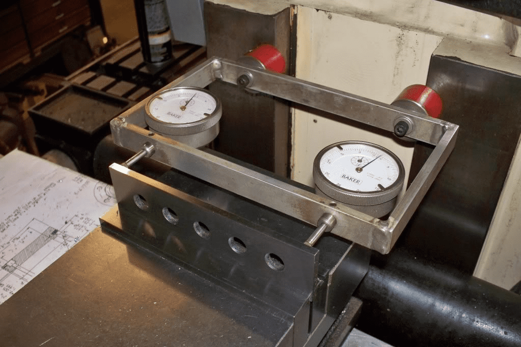 A stainless steel vee block with red anodized knobs and two dial indicators.