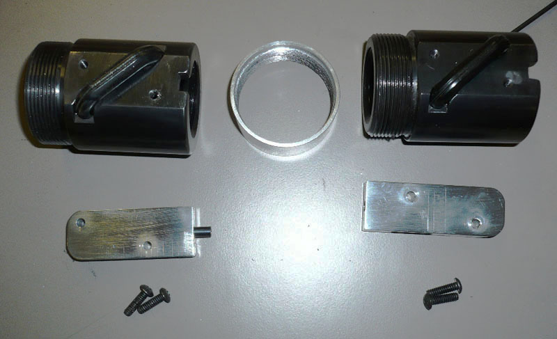 Metal firearm muzzle brake or flash hider components on a flat surface.