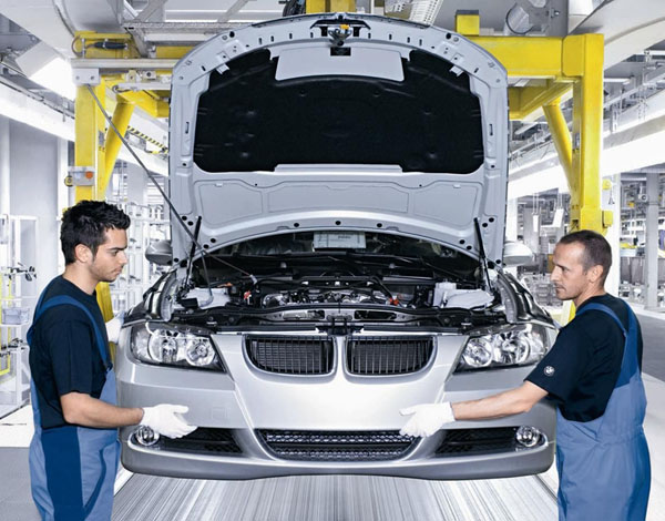 Two men working on a silver BMW in a factory setting.