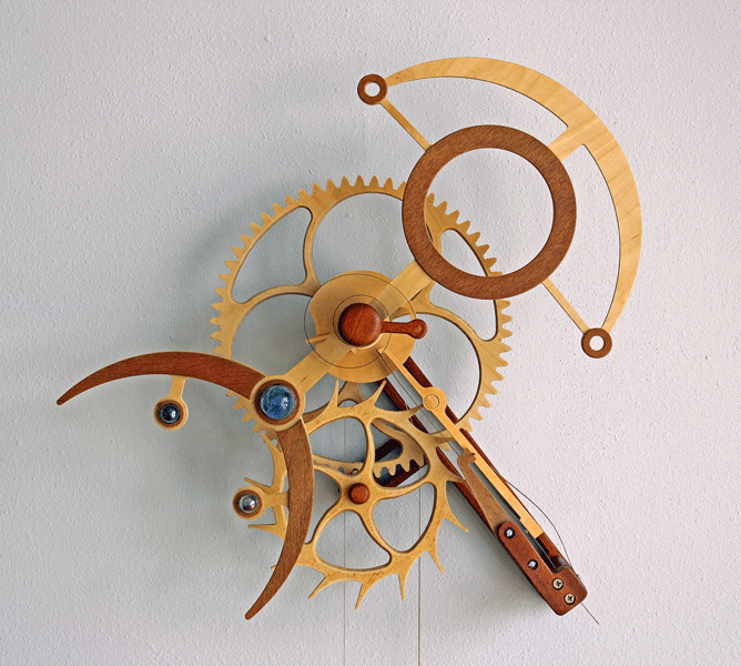 Wooden mechanical device with gears, levers, and other components on a light gray background.