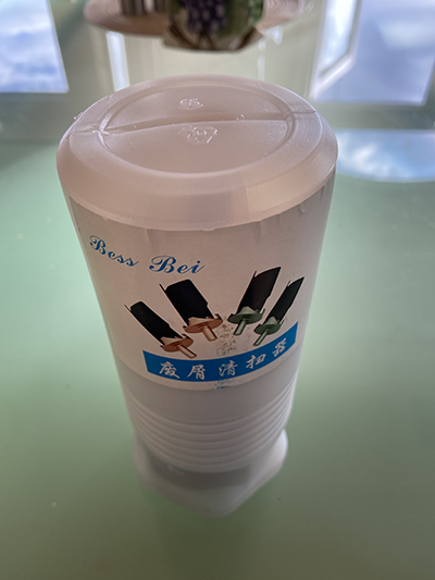 White cup with "Boss Rei" text and three tools on a reflective surface near machine shop/metal fabrication setting.