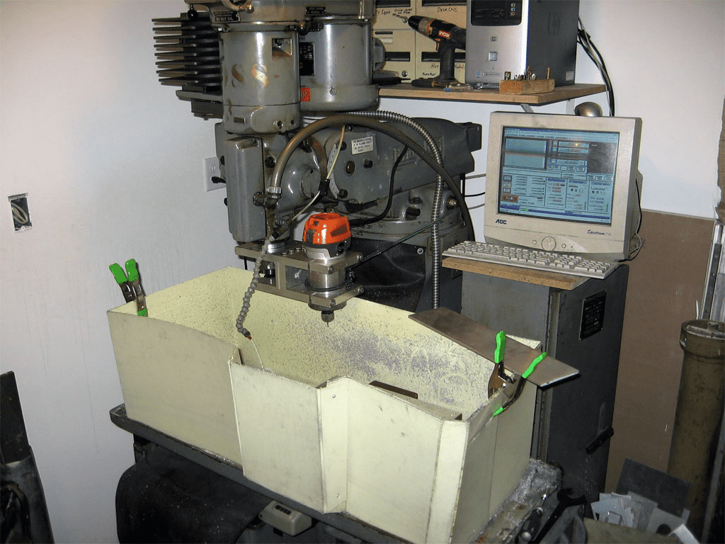 Industrial metalworking setup with computer monitor displaying software interface, a large milling machine and various tools and machinery in the background.