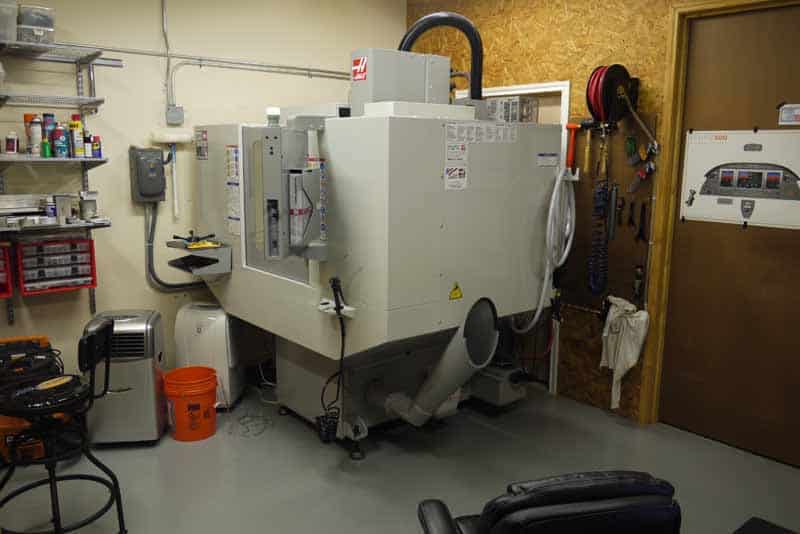 Well-equipped machine shop with CNC machines, toolboxes, and fabrication equipment, amidst dust and debris.