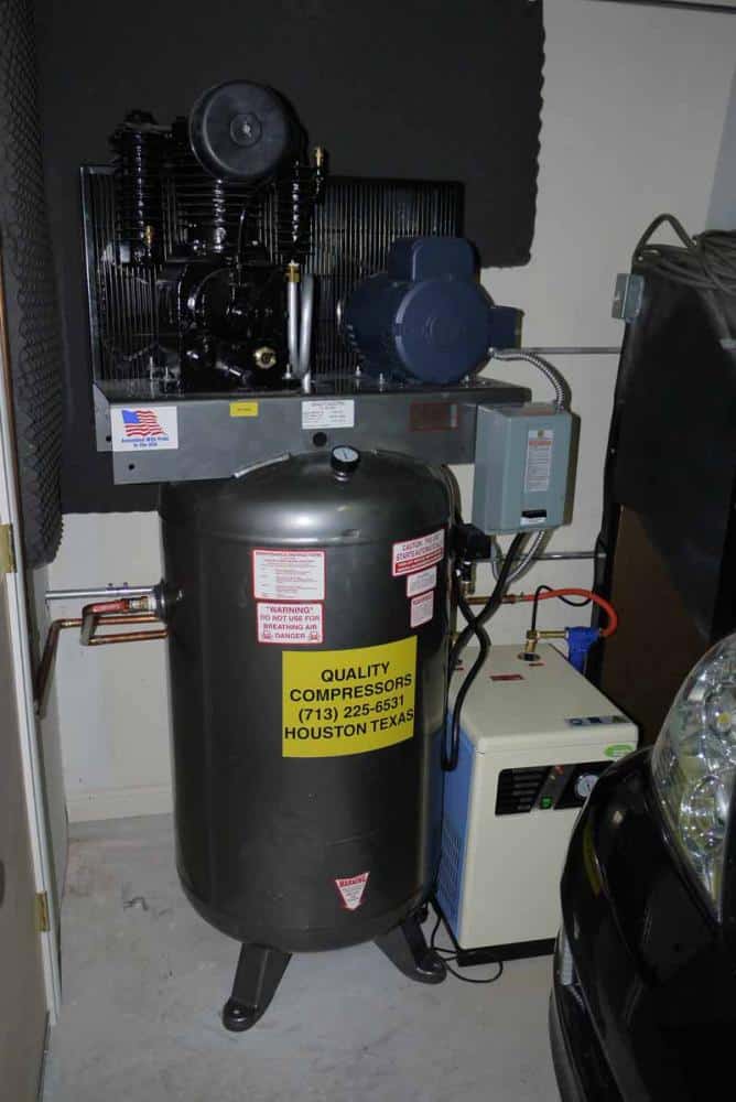 Industrial air compressor in a garage or storage room surrounded by pipes and wires.