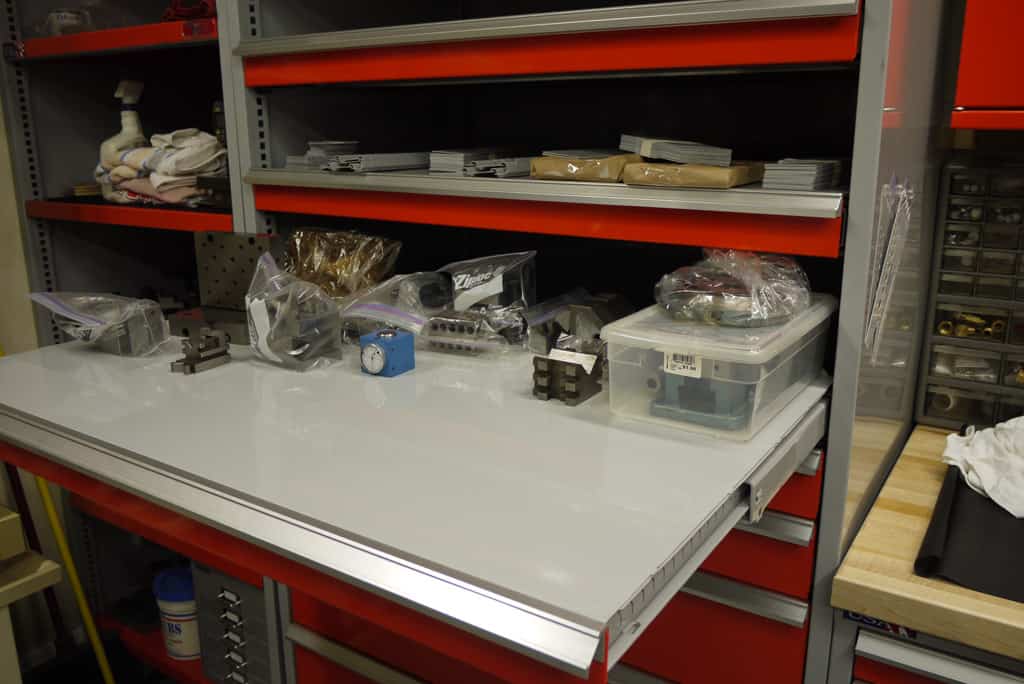 Cluttered workbench with tools and materials scattered across a white metal-worked surface.
