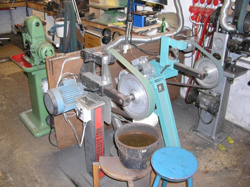 A cluttered workshop with machinery, grinders, sanders, and various metalworking equipment.