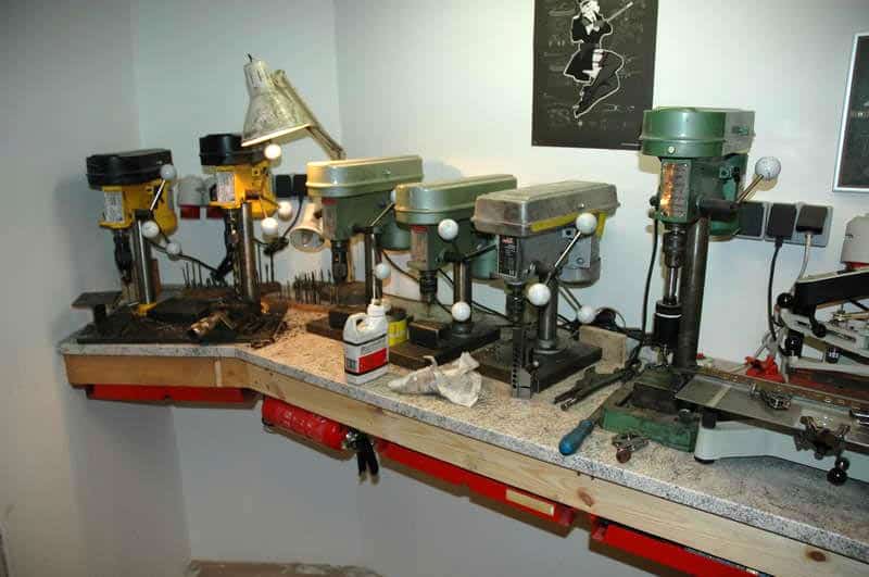Well-organized workshop with three drill presses on a gray countertop and various tools and equipment below.
