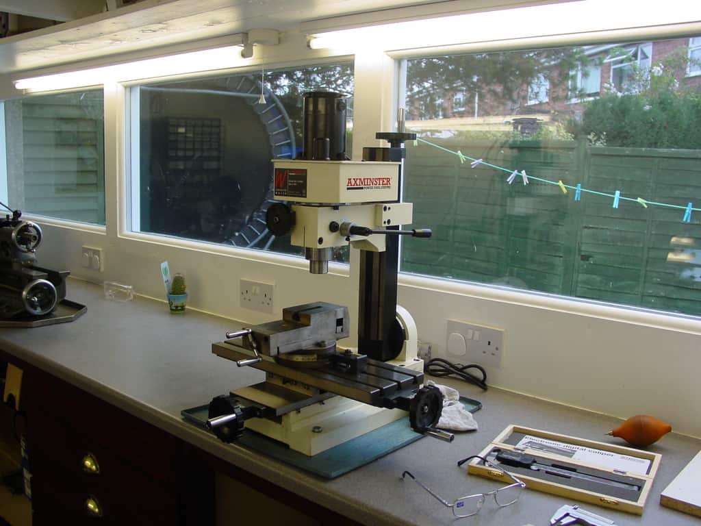 A well-lit workshop with workbench, drill press, milling machine, lathe, and various hand tools.