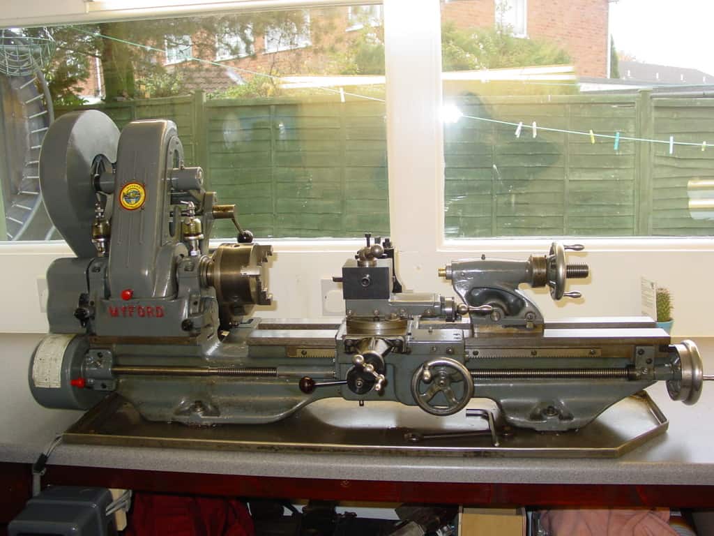Old lathe on countertop with wheel and "MILFORD" logo, against a fence backdrop.