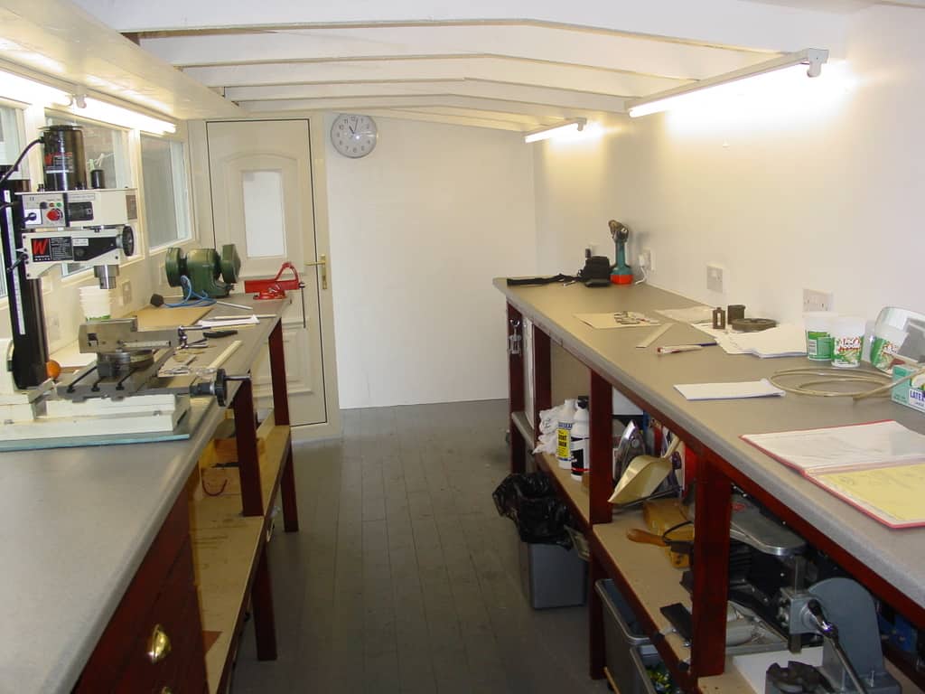 Two cluttered workbenches with various tools and equipment for metal fabrication in a well-lit room.