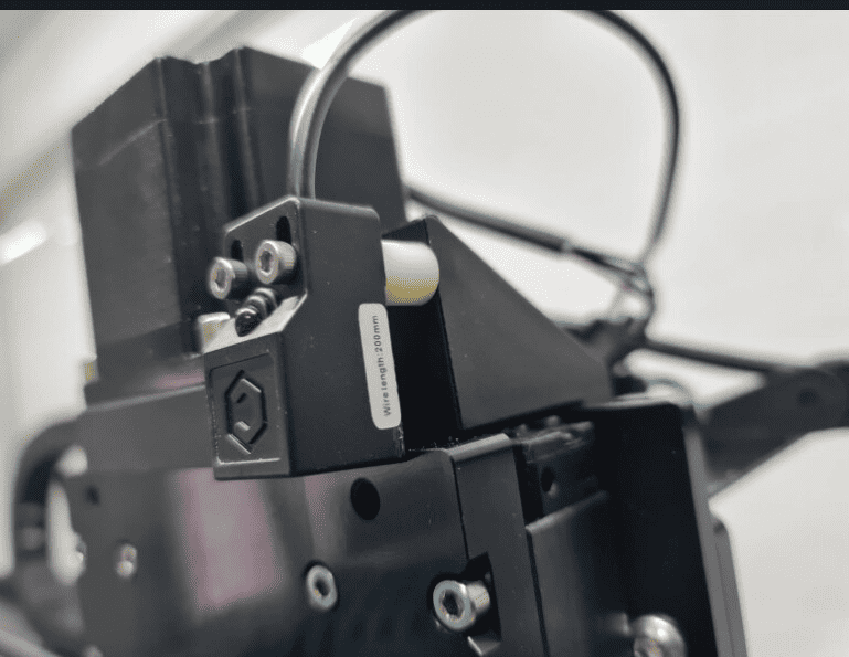 Black metal object with hexagonal nut and illegible text stickers.